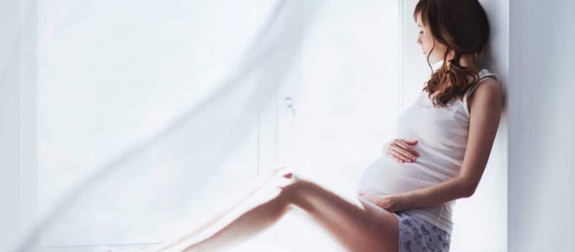 young pregnant woman sitting on the window